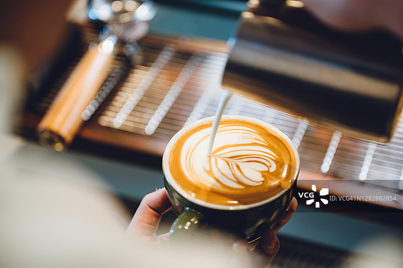 咖啡师制作拉花艺术，镜头聚焦在杯中的牛奶和咖啡，复古滤镜图像图片素材