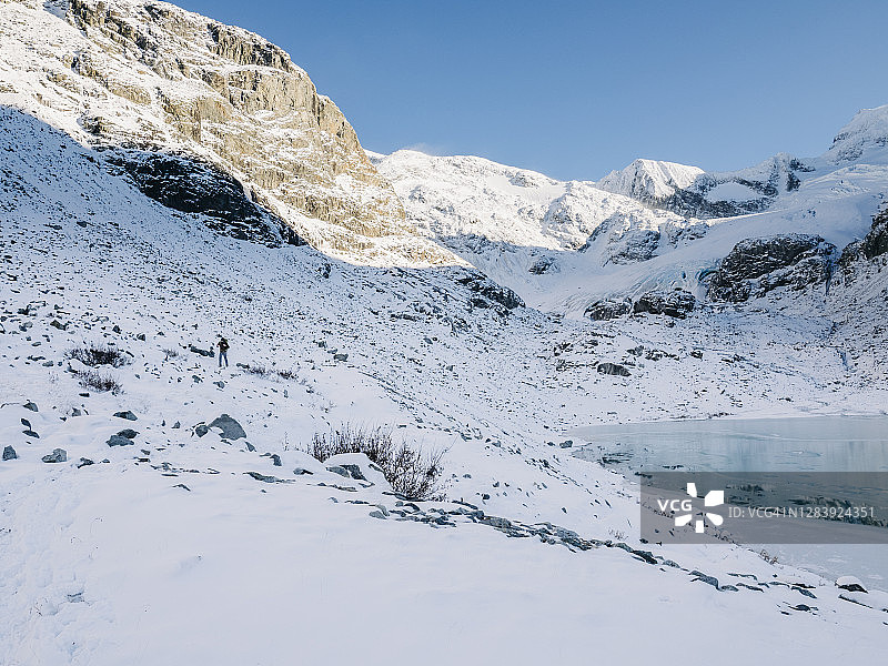登山者在寒冷的雪地里徒步行走，沿着部分结冰的高山湖泊的海岸图片素材