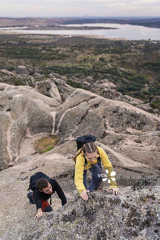 一对年轻的夫妇在艰难的徒步路线上帮助对方在困难的攀登。图片素材