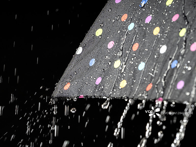打开的伞上有雨滴从天空中落下在黑色的背景上。图片素材