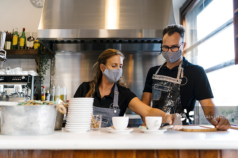 2019冠状病毒病期间，咖啡店的男、女咖啡师戴着防护口罩工作图片素材
