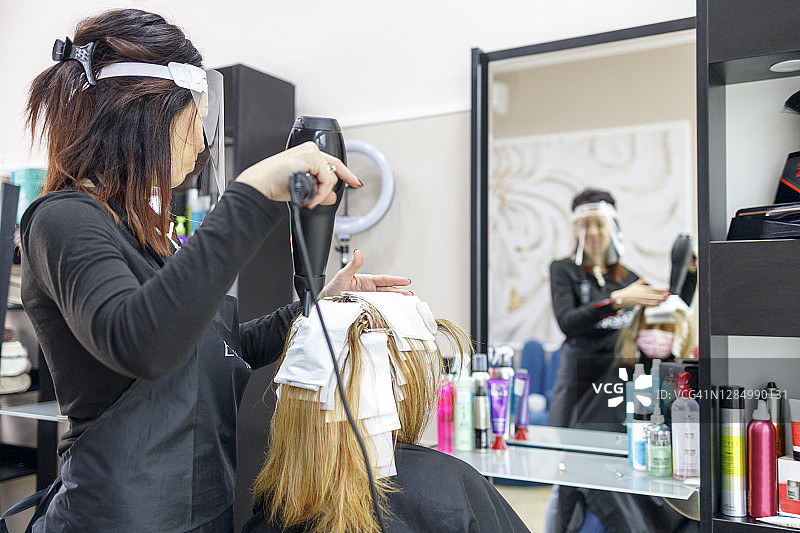 发型师使用吹风机来加热客户头发上的箔片，突出头发图片素材