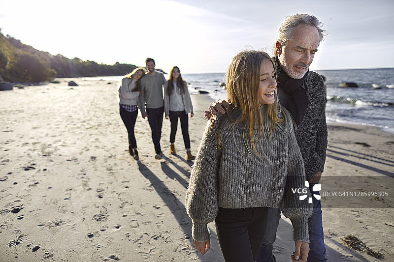 父亲和女儿在海滩上散步，背景是家人图片素材