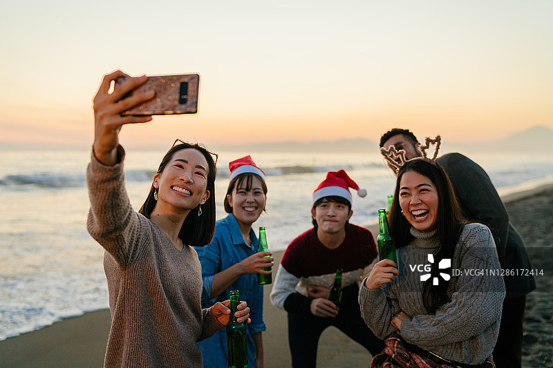 一群朋友在海滩上享受圣诞派对，用智能手机自拍图片素材