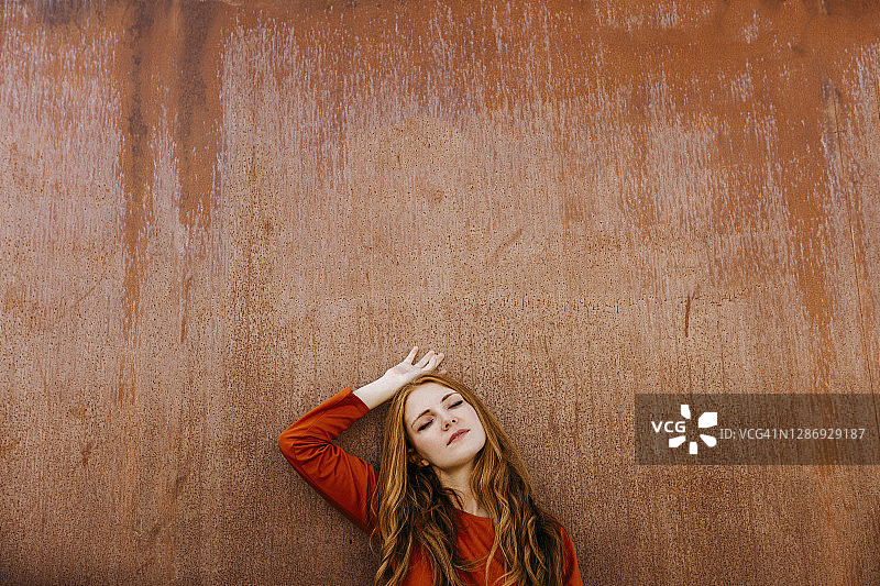 年轻女子闭着眼睛靠在棕色的墙上图片素材