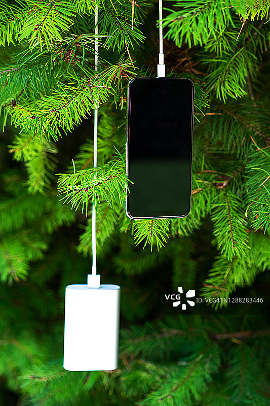移动智能手机无线充电，通过共享电池的设备在圣诞树的背景。图片素材