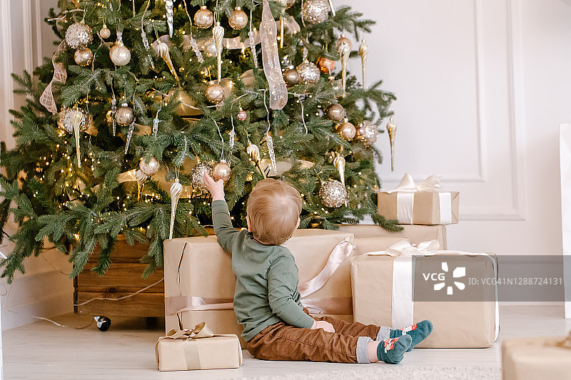男孩坐在圣诞树下拿着礼物图片素材