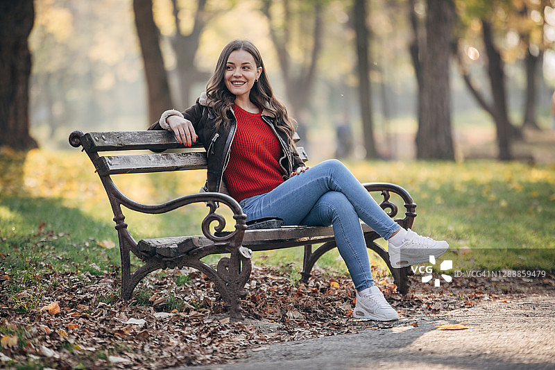 一位美丽的年轻女子在秋季公园的长椅上休息图片素材