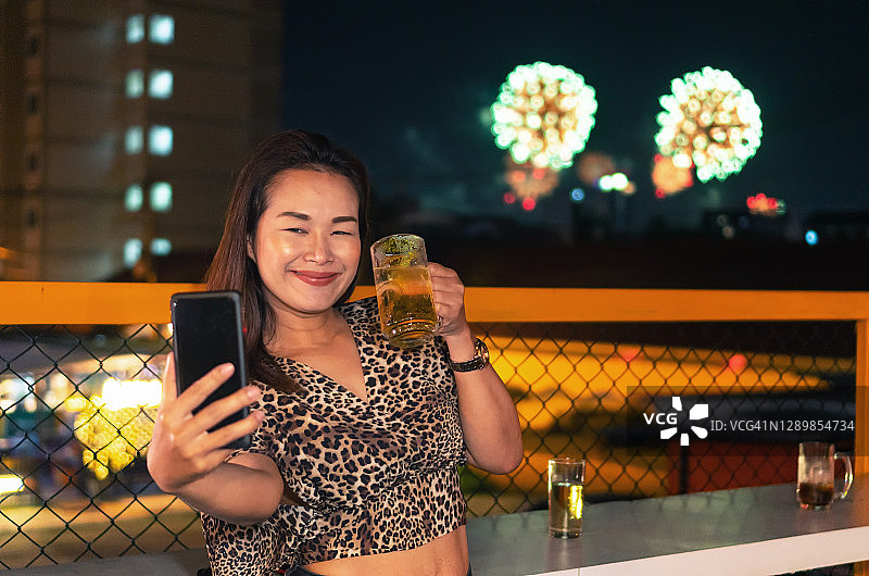 亚洲女人在烟花背景下喝着啤酒自拍图片素材