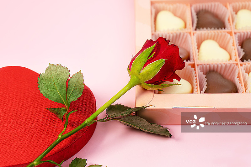 粉色背景下的情人节红玫瑰、心形盒子和巧克力糖果。图片素材