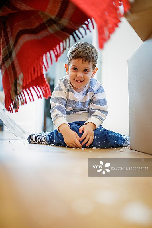 快乐的幼儿，坐在拼花地板上躲在纸板箱旁图片素材