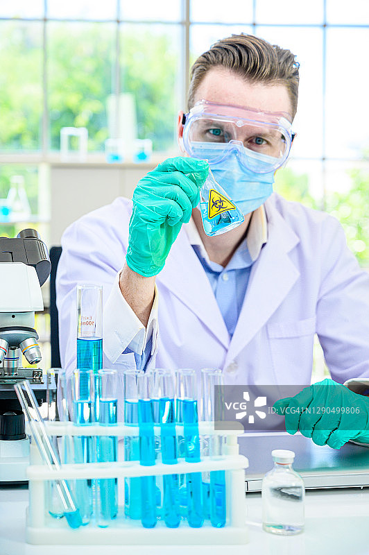 男科学家穿着防护服，拿着烧杯或管，里面装着样品液体，在实验室里使用许多实验室设备进行研究。图片素材