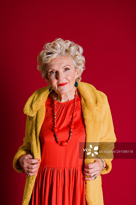 一位有着金色短卷发的老妇人穿着红色的长裙，穿着黄色的皮大衣图片素材
