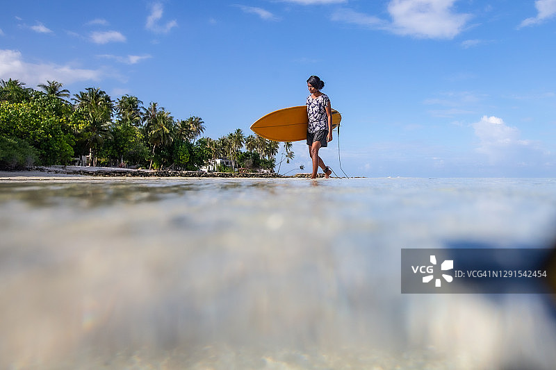 冲浪者在海浪中度过一段时间后走回一个热带岛屿图片素材