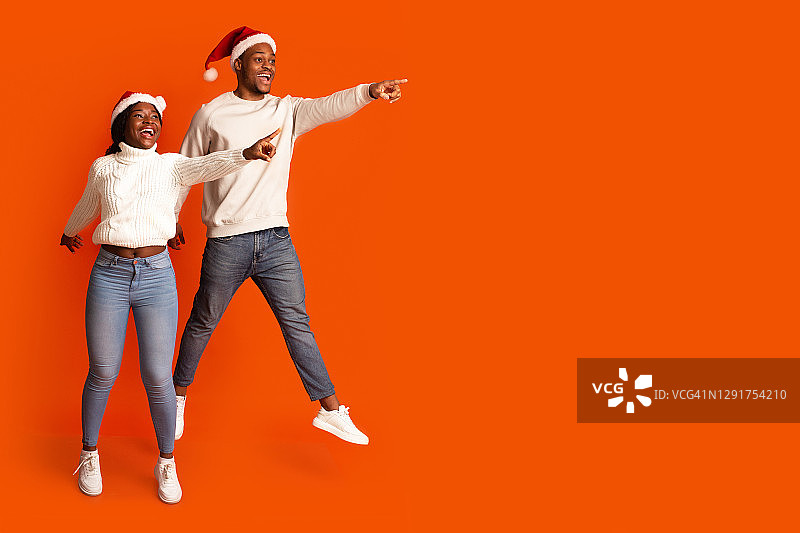 看那里。戴着圣诞老人帽的快乐黑人夫妇跳着指着一边图片素材