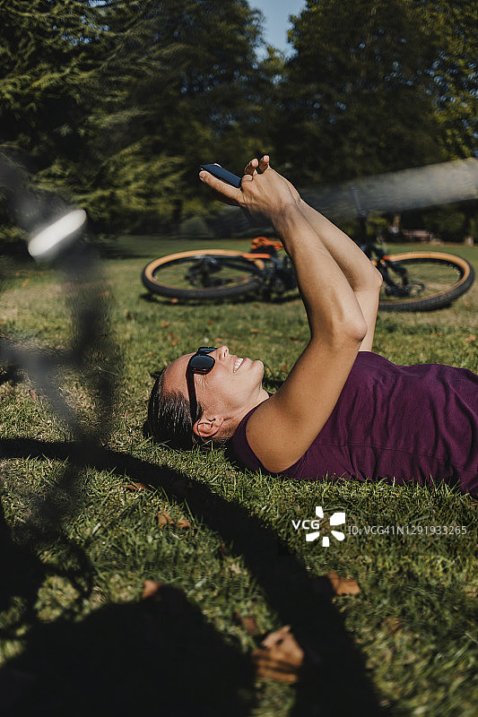 女运动员在公园里骑着电动山地车躺在草地上玩手机图片素材
