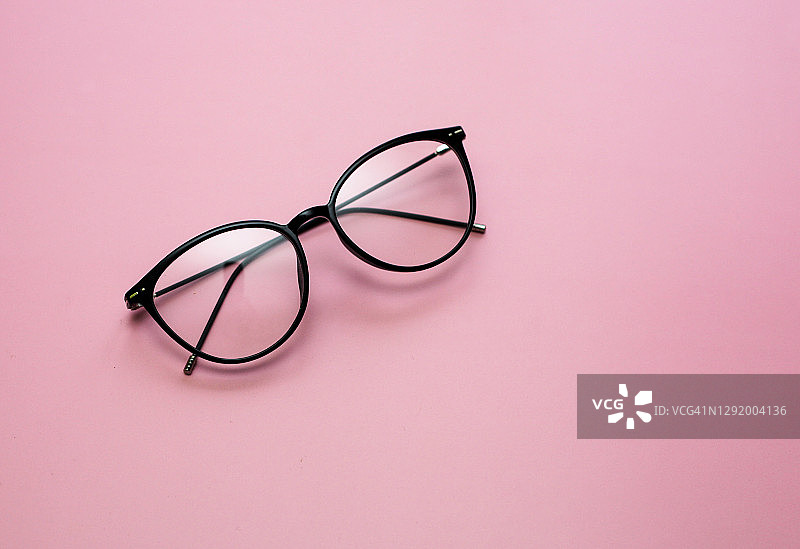 时尚的现代眼镜在粉红色的背景。风格、时尚、办公、学习、工作的概念。图片素材