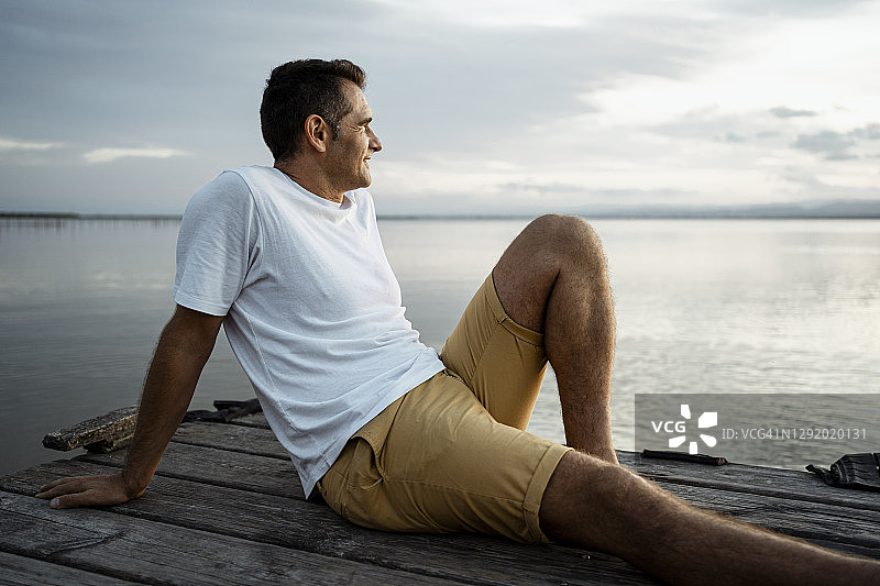成熟的男人坐在湖边的防波堤上，对着天空打发闲暇时光图片素材