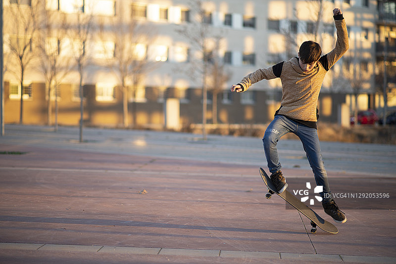 年轻的白人少年在红色小屋在城市里跳滑板图片素材