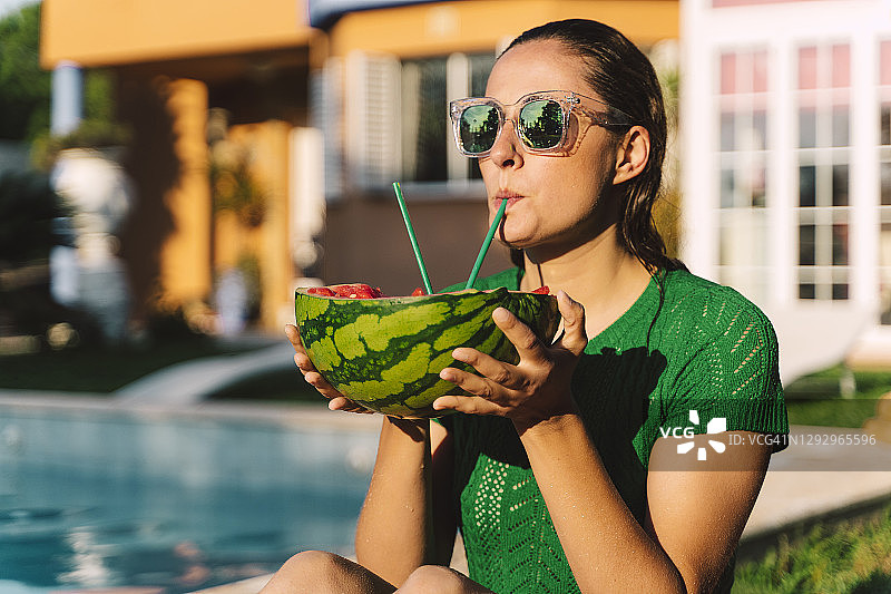一个女人在游泳池边用西瓜吸管喝水图片素材