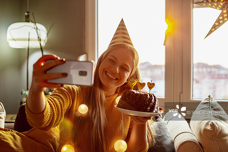 年轻女子庆祝生日，并与生日蛋糕自拍图片素材