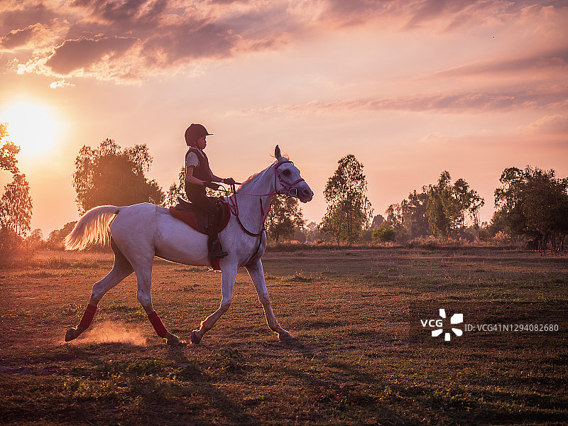 年轻的亚洲女孩喜欢在田野骑马，剪影骑手日落的背景图片素材