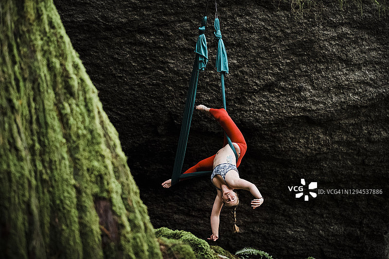 女杂技演员在黑暗的森林里的空中吊床上表演倒立的身体动作图片素材
