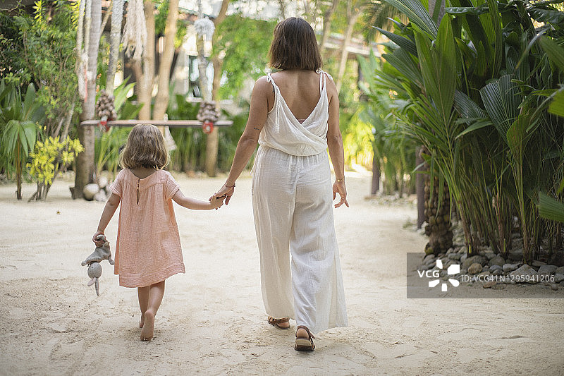 母亲和女儿手牵着手在热带度假村散步图片素材