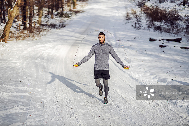 雪天，健硕的运动员在大自然的小径上跳绳。健康习惯，冬季健身图片素材