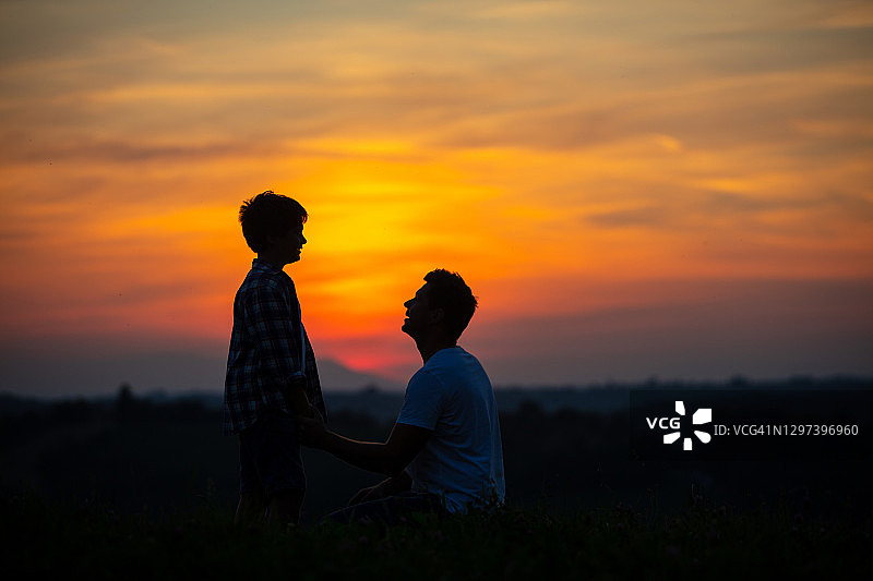 日落时分，父亲和儿子在草地上聊天图片素材