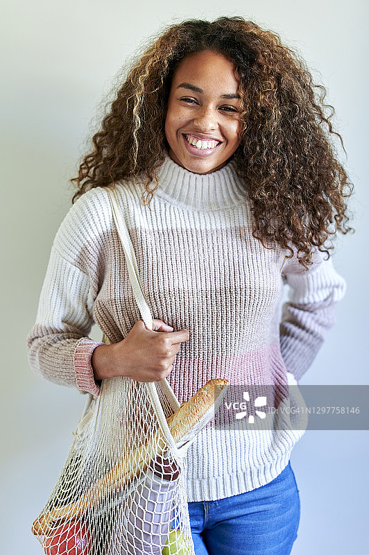 微笑的年轻女子与杂货店购物袋靠白墙图片素材