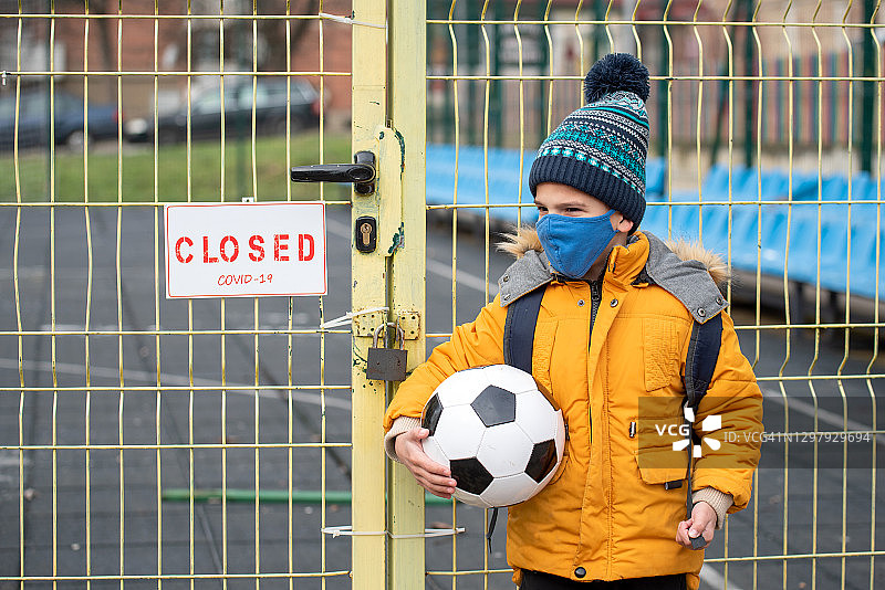 一名小男孩站在因冠状病毒大流行而关闭的游乐场前图片素材