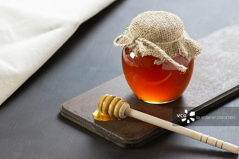 有机新鲜液体蜂蜜在玻璃罐中与勺子在乡村背景，健康食品图片素材