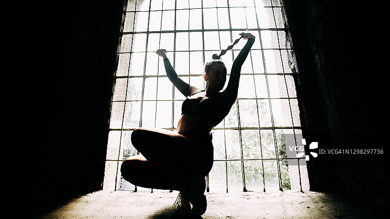年轻女舞者在背光工作室练习。窗台上的剪影图片素材