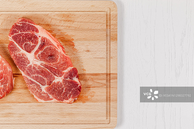 新鲜的生猪肉排放在坚实的山毛榉木砧板上，放在白色的桌子上图片素材