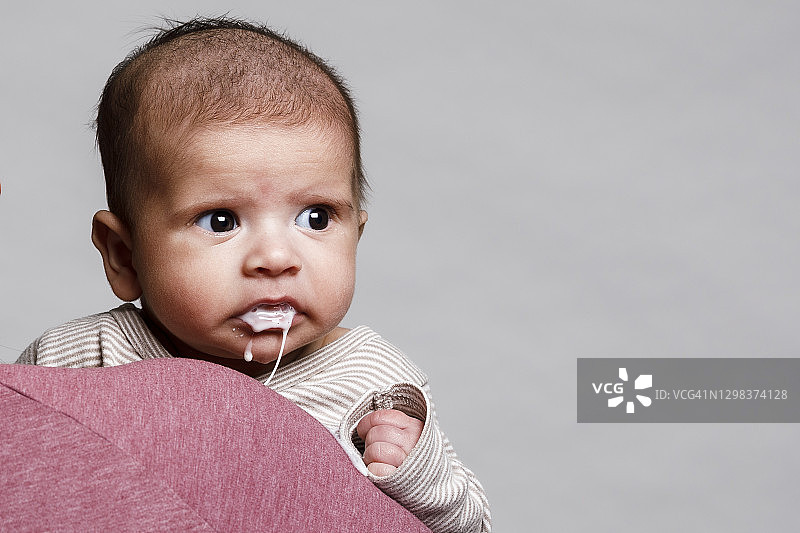 一名男婴被母亲抱在怀里，嘴里吐出了奶粉，凝视着图片素材