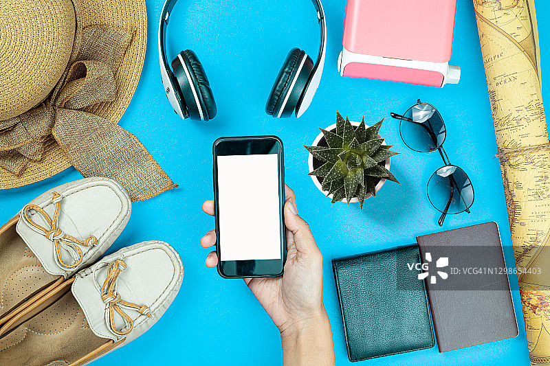 把手持智能手机的人夹在旅行配件护照、包、眼镜、相机放在木桌上。暑假旅游概念。图片素材