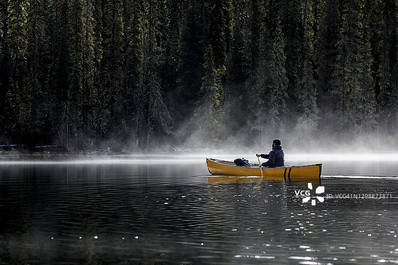 在一个阳光明媚的日子里，一名专注的男子在雾蒙蒙的湖面上驾驶着独木舟图片素材