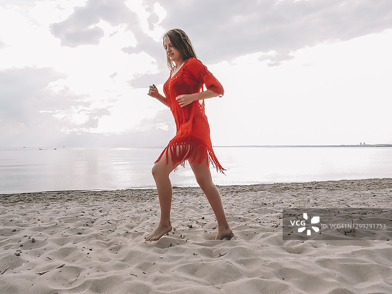 一名晒黑的年轻女子穿着红色短裙，身材苗条，在海湾附近的沙滩上跳舞图片素材