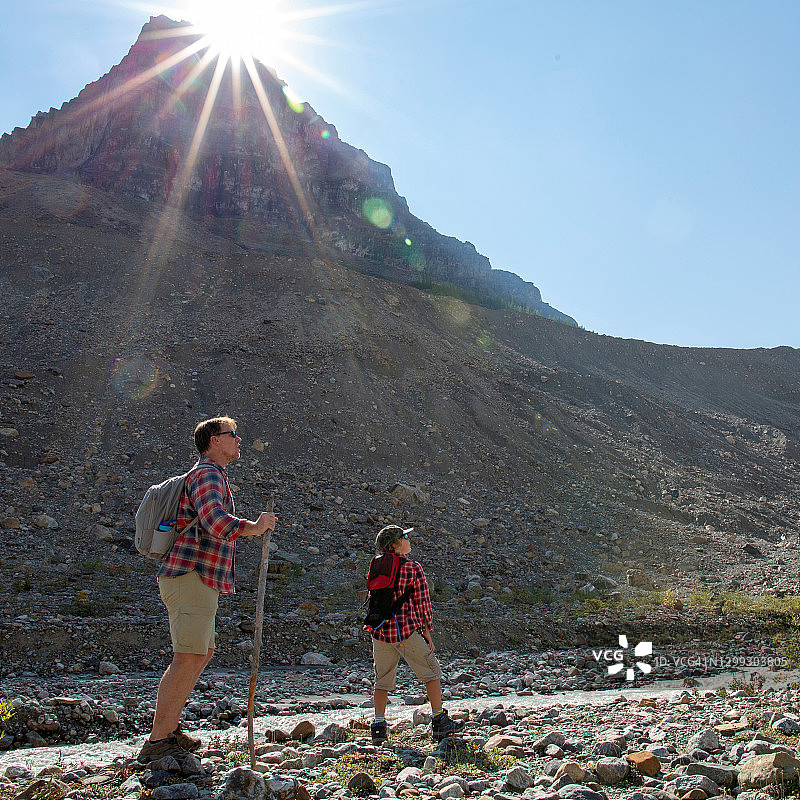 父亲和儿子在早晨沿着阳光明媚的山谷徒步旅行图片素材