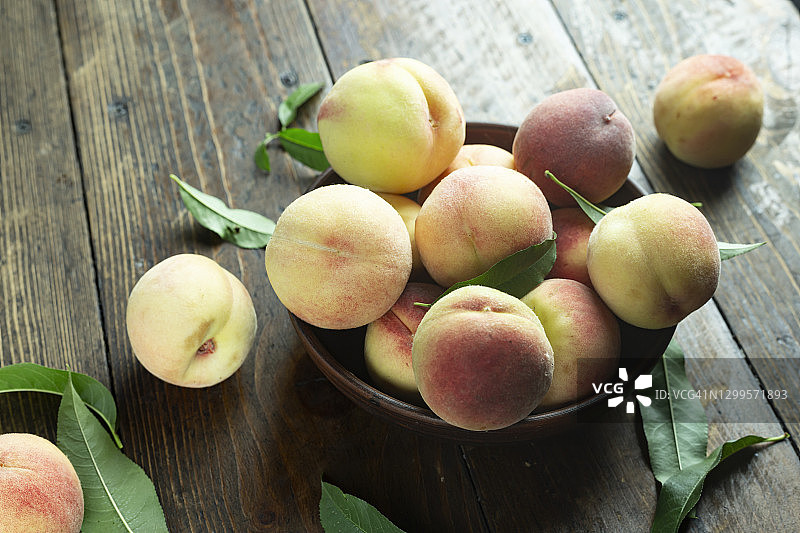 陶土碗里放着新鲜的桃子，放在质朴的木桌上。桃叶存在于成分中。图片素材