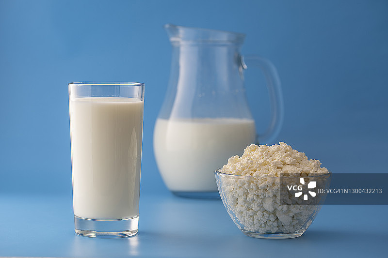 白色的牛奶在一个罐子和玻璃杯和乡村奶酪在蓝色的背景。乳制品产品概念图片素材