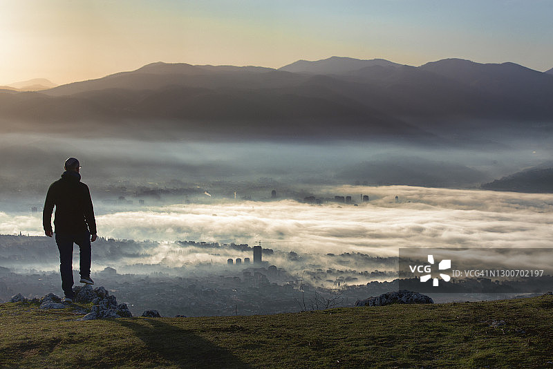一个人的剪影在山顶在黎明看城市在一个雾蒙蒙的黎明图片素材