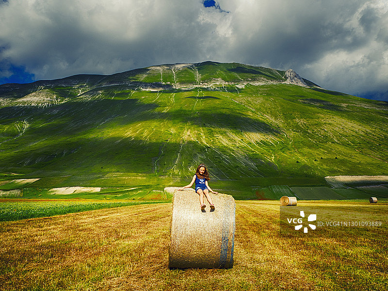 意大利翁布里亚，一个女孩坐在田里的干草堆上图片素材