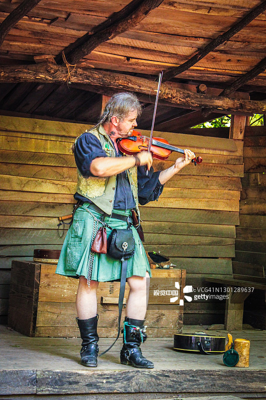 马斯科吉美国人在绿色短裙，带着辫子和袋子在乡村木制舞台上演奏小提琴-动态模糊图片素材