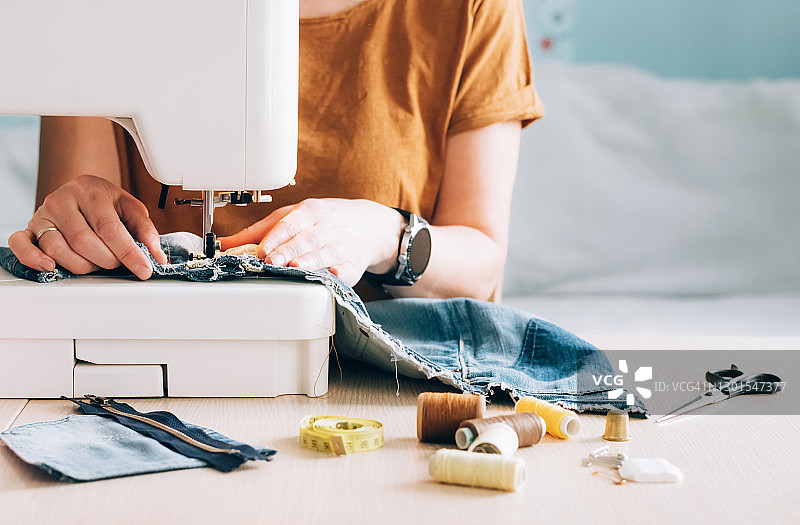 一个在缝纫机上工作的女裁缝用旧斜纹棉布重新缝制图片素材