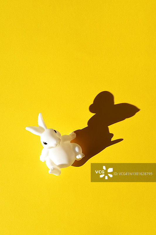 黄色背景上有阴影的白兔玩具。图片素材