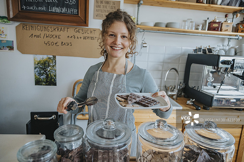 快乐的年轻女店员拿着一盘巧克力站在咖啡馆图片素材