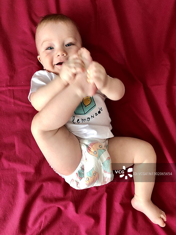 开心的小男孩穿着婴儿尿布躺在床上，选择性的专注图片素材