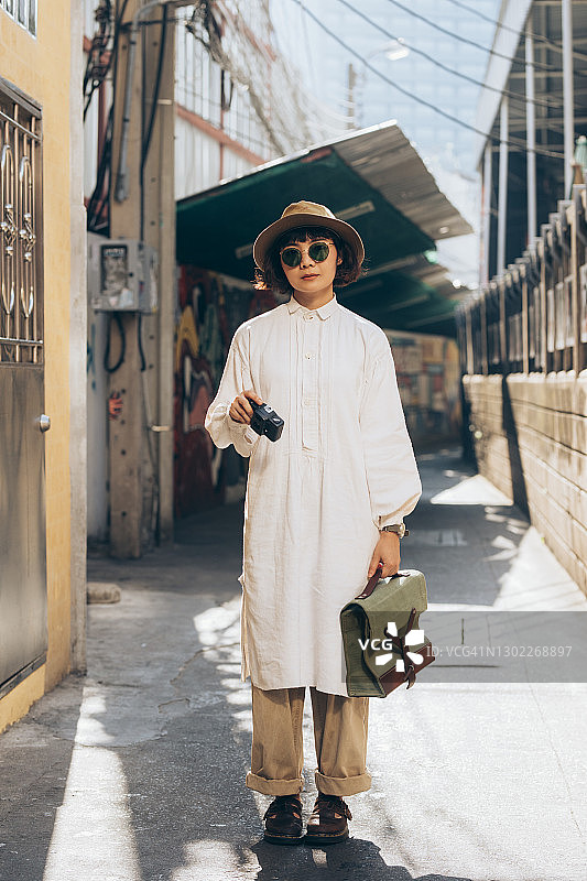 年轻的泰国妇女站在街上，穿着白色和拿着她的相机图片素材